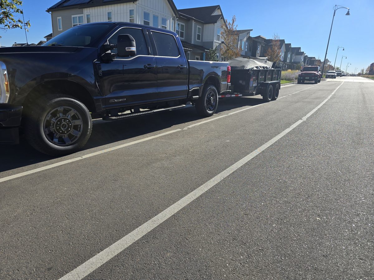 Northern Colorado Junk Removal truck towing a covered loaded trailer through a neighborhood